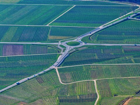 Aerial view of a roundabout intersecting roads amid a patchwork of vineyards and fields, creating a symphony of greens and browns, Mittelwihr, Grand Est, France.