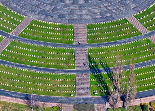 Aerial view of aligned tombstones in a circular war memorial, where green grass meets stone pathways, creating a serene and somber landscape, Mittelwihr, Grand Est, France.