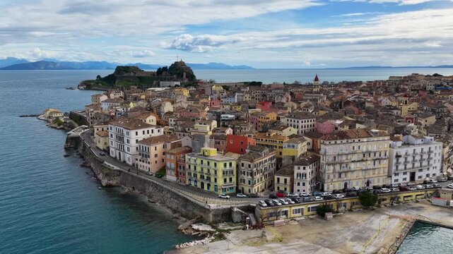 Aerial view of the colorful Venetian architecture in Corfu Old Town, Greece, featuring the historic Old Fortress, calm Mediterranean sea, and vibrant cityscape under a cloudy sky during the day