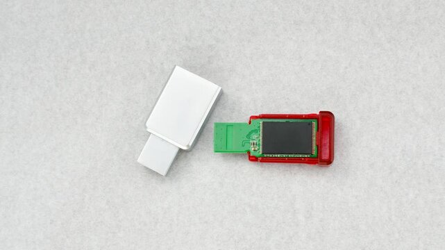 Close-up of a disassembled USB flash drive on a white background, revealing its internal complexity. Close-up of an open USB flash drive, exposing circuits and connections, on a white surface.