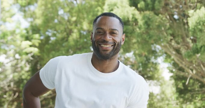 Man is laughing and leaning forward with hand on hip in sunlit green tree canopy