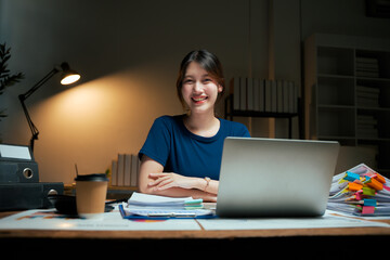 Fototapeta premium Young woman smiling while working late at desk