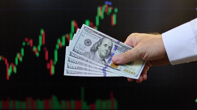 Close up view of man hands, American dollar banknotes, market chart on computer screen in background. Concept of currency growth, stock price change, volatile financial market, internet trading in USA