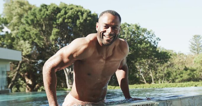 African American man pressing down pushing up on coping exiting home pool in pink trunks laughing