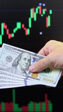 Close up view of man hands, American dollar banknotes, market chart on computer screen in background. Concept of currency growth, stock price change, volatile financial market, internet trading in USA