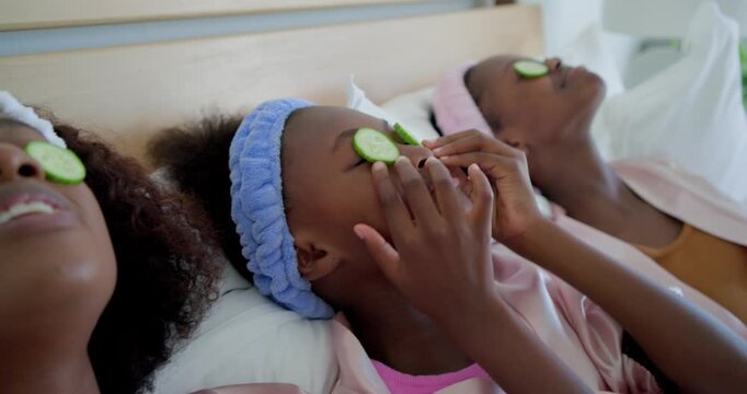 African American females lying on bed placing cucumber slices over eyes after mom's smile for spa