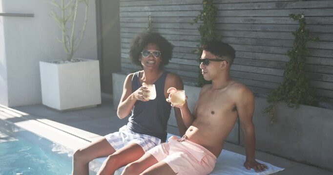 African American male friends on towel poolside, raising drinks and clinking glasses, toasting bond