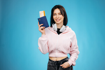 Excited female tourist holding passport and airline tickets isolated on blue background. Travel and...