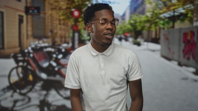 Young african american man with glasses hand covers mouth on city street with parked bicycles; surprise.