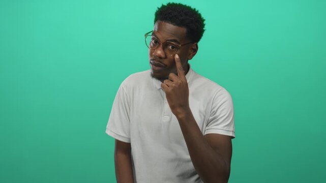 Young man finger pointing to eyeglasses in bright green studio set showcasing eyewear accessory; clarity focus.