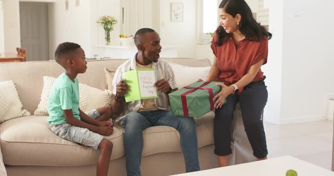 Father reading Happy Father's Day card mother handing wrapped gift family celebrating for marketing