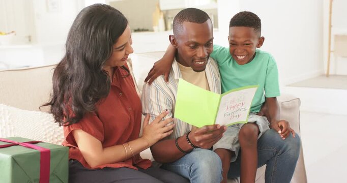 Family celebrating on couch, father holding card, reading, child hugging, mother touching, gift