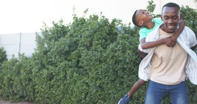 Father and son child giving piggyback with son jumping up, wrapping arms, walking hedge-lined path