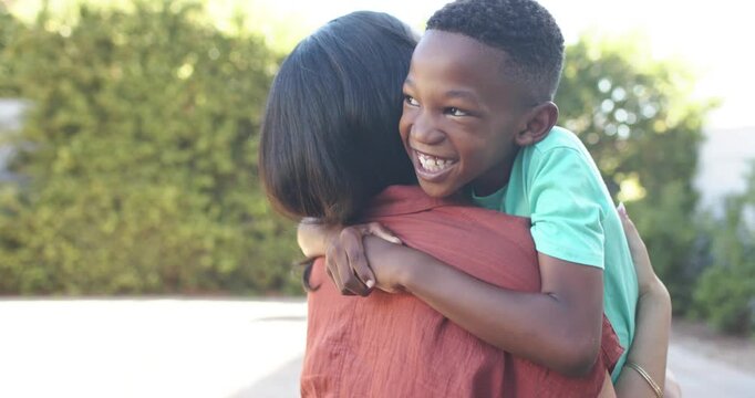 Diverse mom and son laughing, boy clinging, mom adjusting hold on driveway, mint shirt rust top