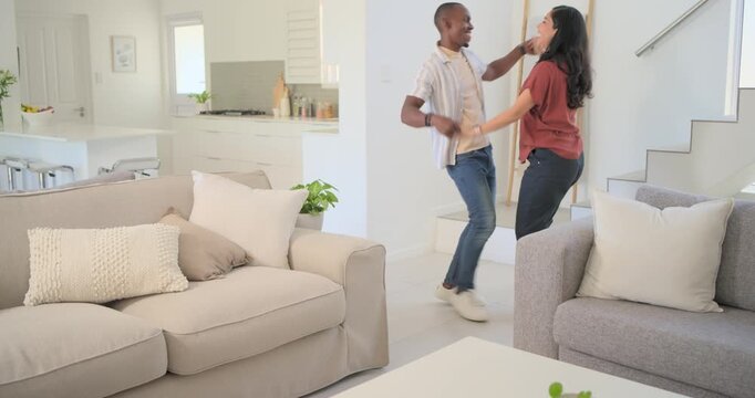 Diverse couple clasping hands and dancing playfully by coffee table near landing, copy space