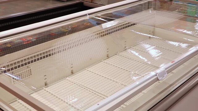 Empty supermarket refrigerator freezer display with no products. Retail shortage concept showing lack of food supply, crisis logistics disruption and consumer panic buying impact on grocery store shel