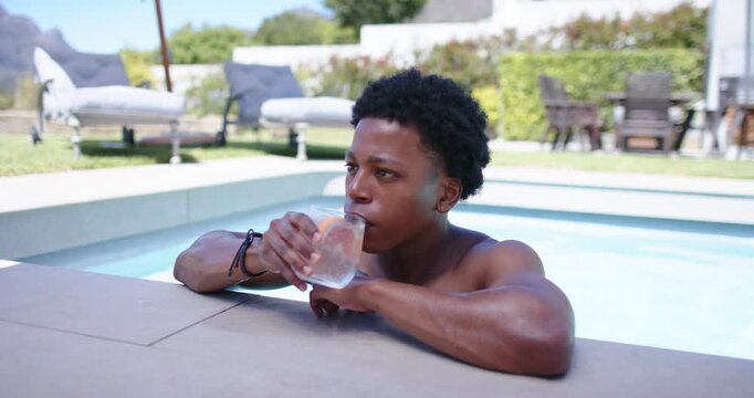 African American man feeling warm from sunlight, sipping then sliding citrus glass on pool coping