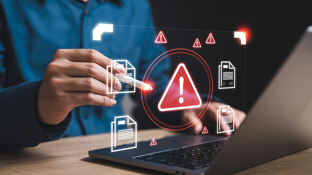 User interacting with laptop displaying virtual security warning symbols and document files for cyber risk management
