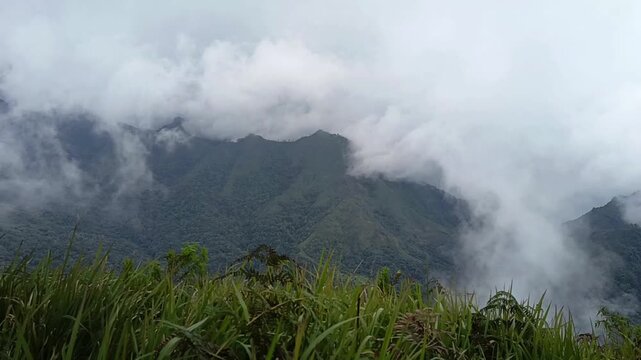 A wide, cinematic view of clouds and thick fog rolling over a deep green valley and mountain ridges. Dramatic and atmospheric nature landscape.