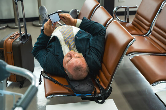 Elderly businessman lying on airport seats and using phone while delay flight