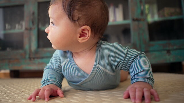 Baby lying on mat indoors, looking to the side with curiosity, supporting upper body during tummy time, early development, strengthening muscles, engaged expression