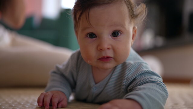 Baby lying on mat indoors, lifting head with curious expression, observing surroundings, early childhood development, strengthening muscles, engaging in tummy time