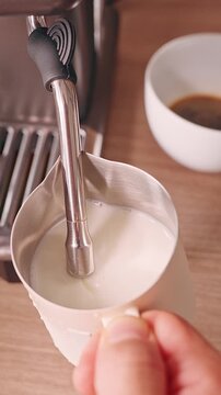 Vertical video. Steaming Milk In Metal Pitcher With Espresso Machine Steam Wand Creating Smooth Microfoam For Latte Coffee Preparation