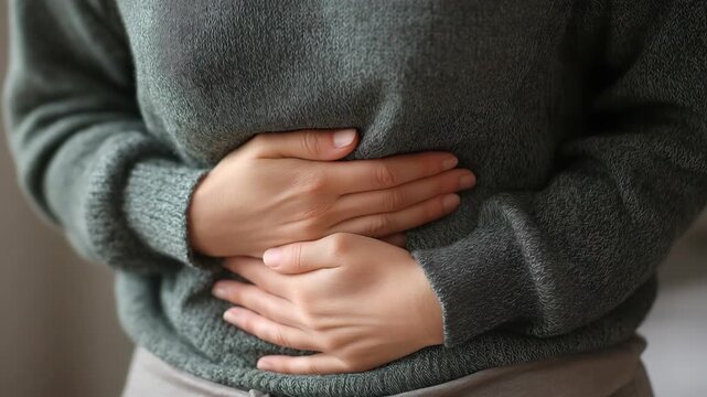  Caucasian woman holding her stomach and taking a deep breath. Concept of abdominal discomfort, digestion problem, stress relief, or breathing exercise for health and wellness awareness.