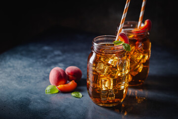 Fototapeta premium Glass of peach or apricot iced tea with fruit slices against dark blue background