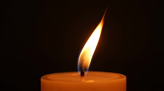 Close up image of a warm glowing candle flame against dark background