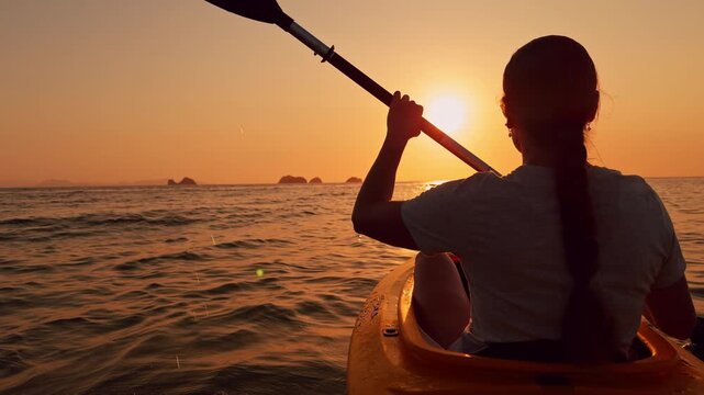 A woman with a long braid paddles a kayak toward the glowing horizon at sunset, slow motion reveals peaceful water and golden sky, sense of freedom and adventure fills the tranquil scene