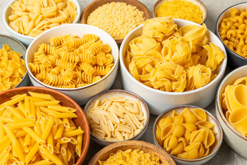 Assortment of uncooked Italian pasta in bowls on background. Variety of dry pasta, top view, food background. Different types of uncooked pasta. ingredients. flat lay. Assorted uncooked Italian pasta 