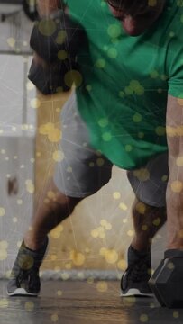 Vertical video: Man performing dumbbell rows in gym, shifting weight for core, yellow mesh overlay