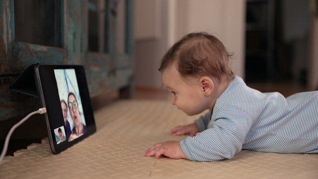 Baby lying on mat closely watching tablet during video call, drooling with excitement, early sensory response, virtual family interaction, technology in daily life