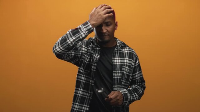 Man holding wrench with hand on forehead in studio, wearing plaid flannel shirt and casual stance, mouth open in exasperated gesture; frustration regret.