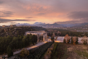 Naklejka premium Aerial view of the ancient Roman theater of Aspendos at sunset near Antalya, Türkiye, surrounded by Mediterranean landscape and dramatic colorful sky.