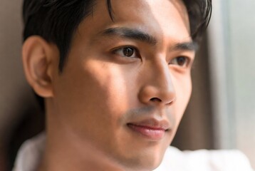 Obraz premium A man with Asian features is gazing thoughtfully out a window.