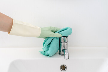 Professional housekeeper wiping chrome faucet with protective gloves