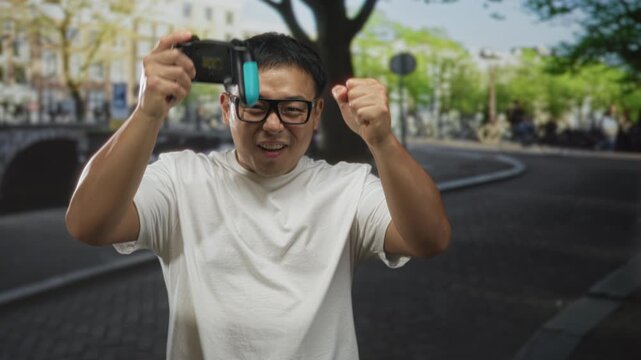 Man gripping game controller and pumping fist on a busy urban street in bright daylight mid afternoon; victory.