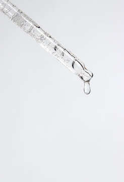 Macro shot of a glass pipette tip forming a single droplet filled with micro-bubbles. Face serum cosmetic beauty product advertising.