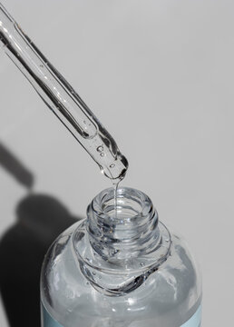 Clear pipette releasing serum into vial against stark grey. Conveys clinical purity and advanced hydration. Ideal for cosmetic advertising and UGC.