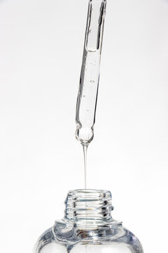 Glass pipette dropping viscous serum into a crystal vial on pure white. Cosmetic ugc
