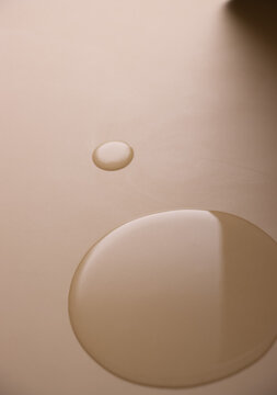 Perfectly smooth pools of clear face serum or oil cosmetic product resting on a matte nude background. Minimalistic cosmetic texture.