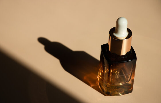 Amber glass dropper bottle with gold collar casting a dramatic elongated shadow. Radiates premium luxury and nighttime recovery. Suited for exclusive anti-aging serum launches, cosmetic ugc