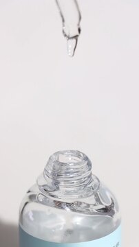 Glass pipette dropping viscous serum into a crystal vial on pure white. Cosmetic ugc