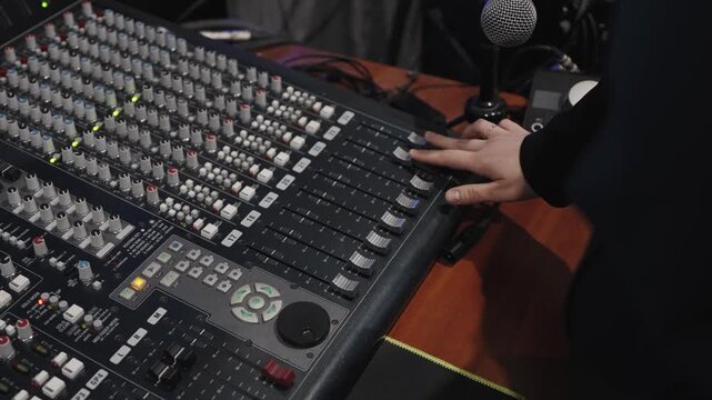 Audio engineer modifying fader positions carefully during recording