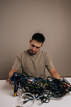 Vertical portrait of frustrated man dealing with a massive pile of tangled electronic cables, facing a complex problem of wire management and technological clutter accumulation