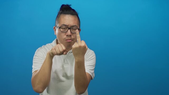 Man showing middle finger and clenched fist in blue studio wearing white polo and glasses; defiance.