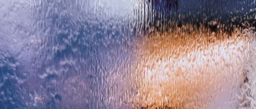 Colorful water flowing over a textured decorative glass panel, forming abstract patterns and shimmering light diffusion. Modern interior design feature with vibrant reflections and calming motion.