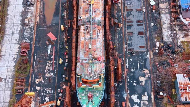 Industrial ship in dry dock for maintenance and repair works. Top view of cargo vessel positioned in shipyard dry dock surrounded by scaffolding and equipment.